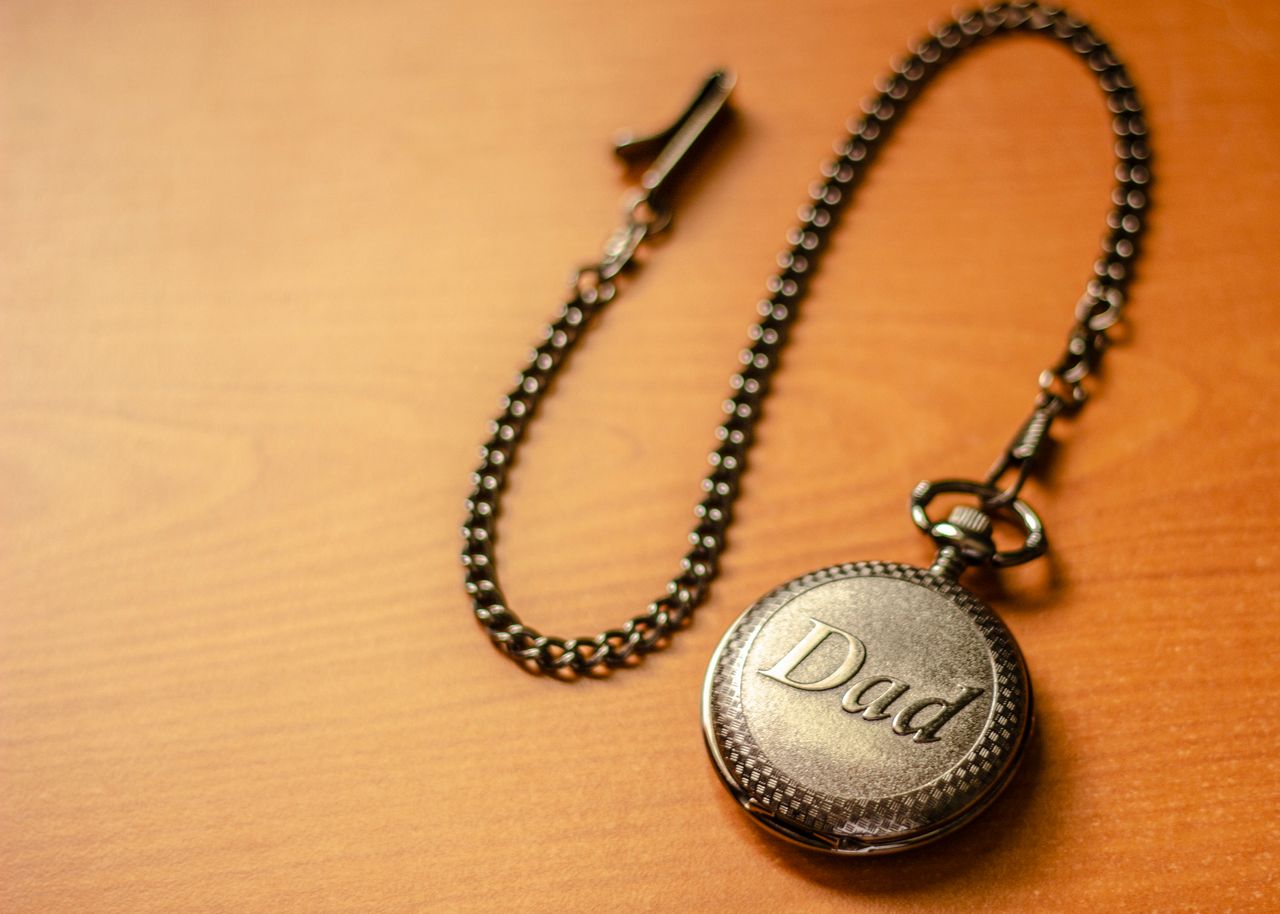 Close-up of a pocket watch with 'Dad' engraving on a wooden surface, symbolizing time and fatherhood.